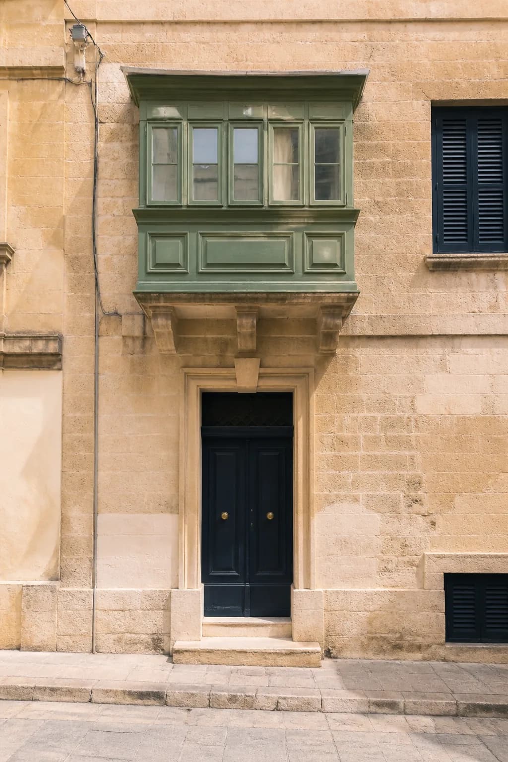 A Maltese limestone townhouse with a green timber balcony above its doorway