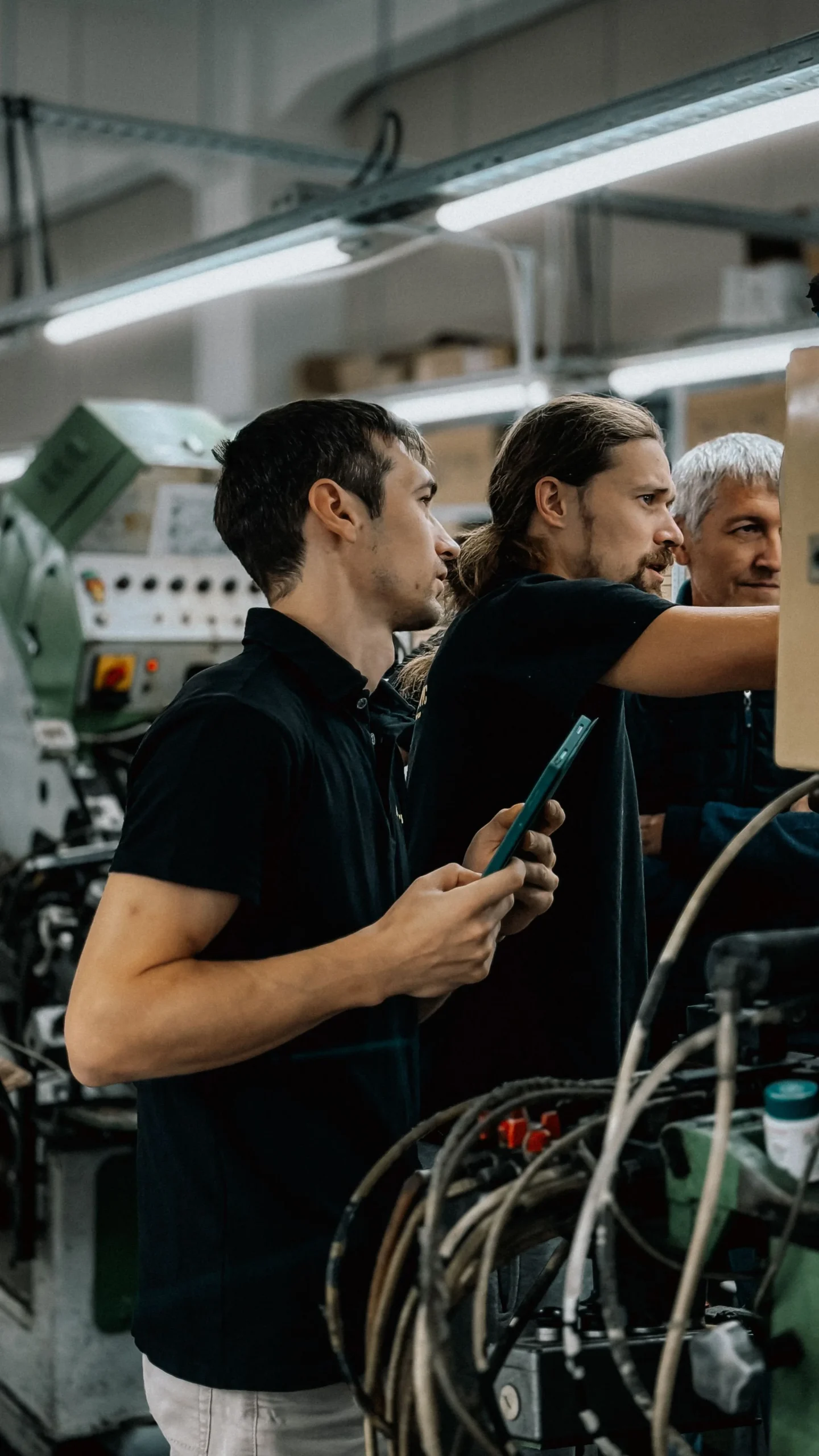 Three colleagues inspecting machinery in a manufacturing workshop